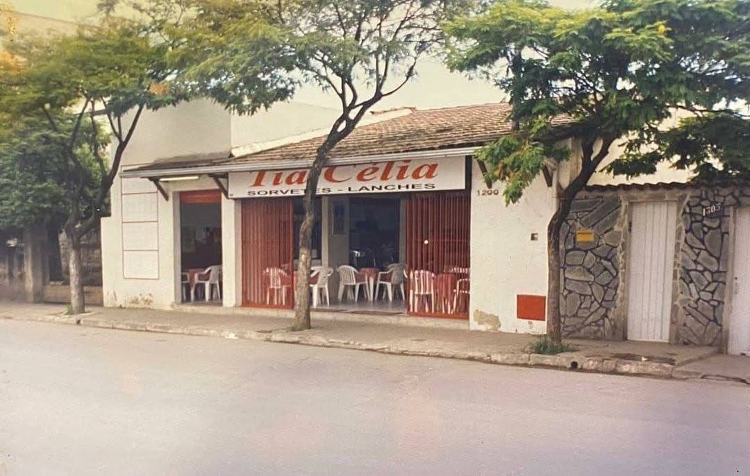 Fotografia antiga da fachada da sorveteria Tia Célia, com mesinhas na calçada e árvores na rua.