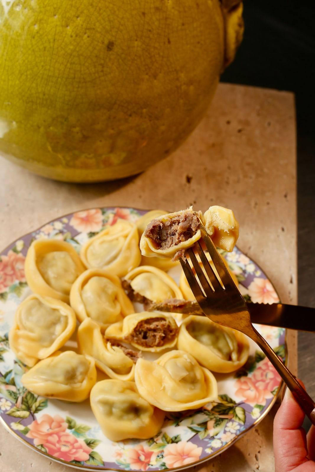 Prato florido com cappelletti de carne, um deles cortado mostrando o recheio.