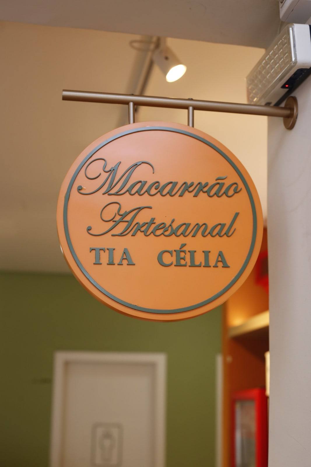 Placa redonda da loja com os dizeres Macarrão Artesanal Tia Célia.